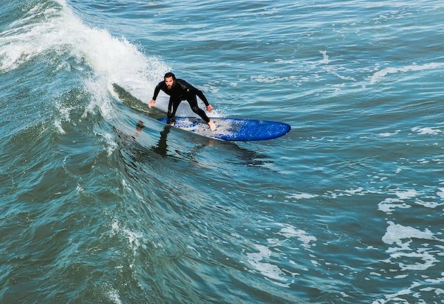 man in wetsuit op surf longboard